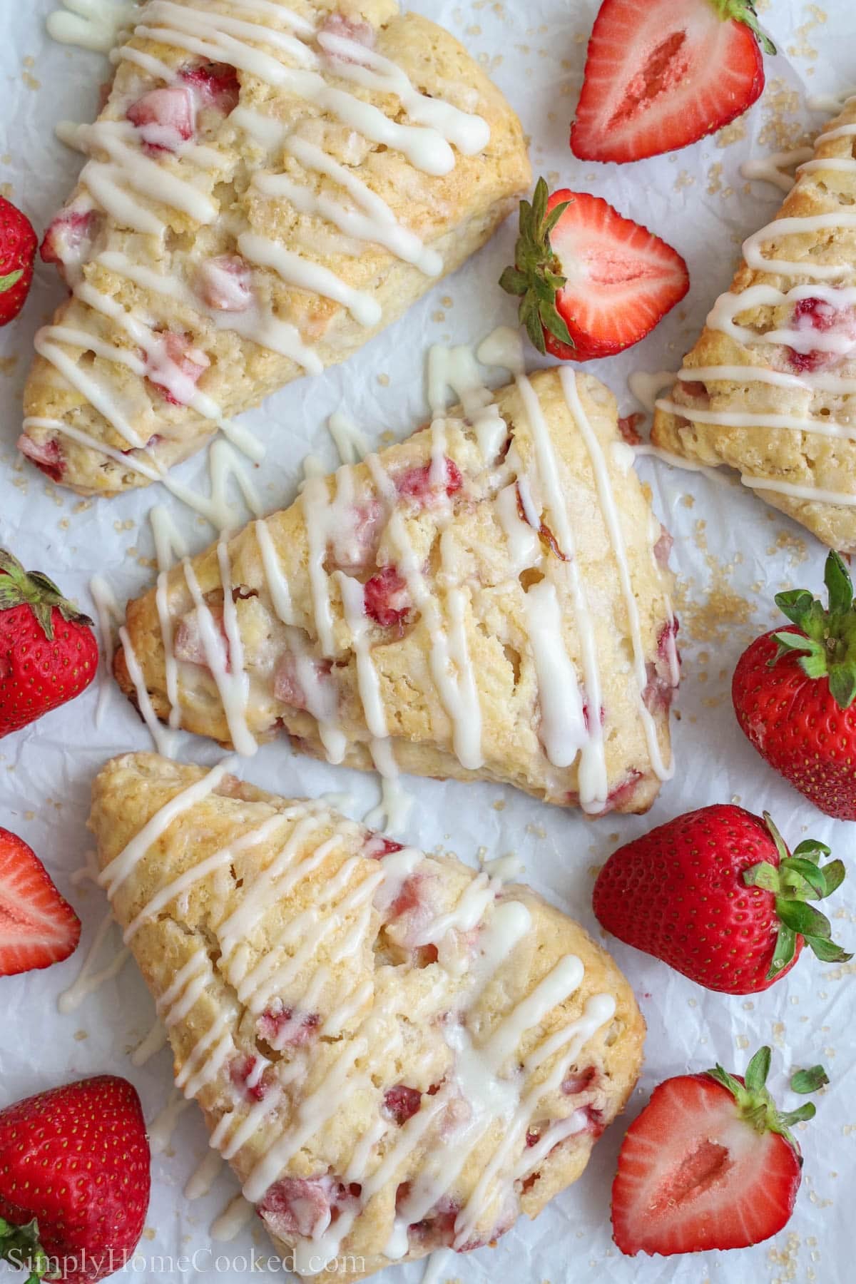 Strawberry Scones on parchment paper with strawberries and glaze drizzled on top.